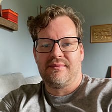Individual named Benjamin Berry - sporting glasses, a beard, and a gray shirt.